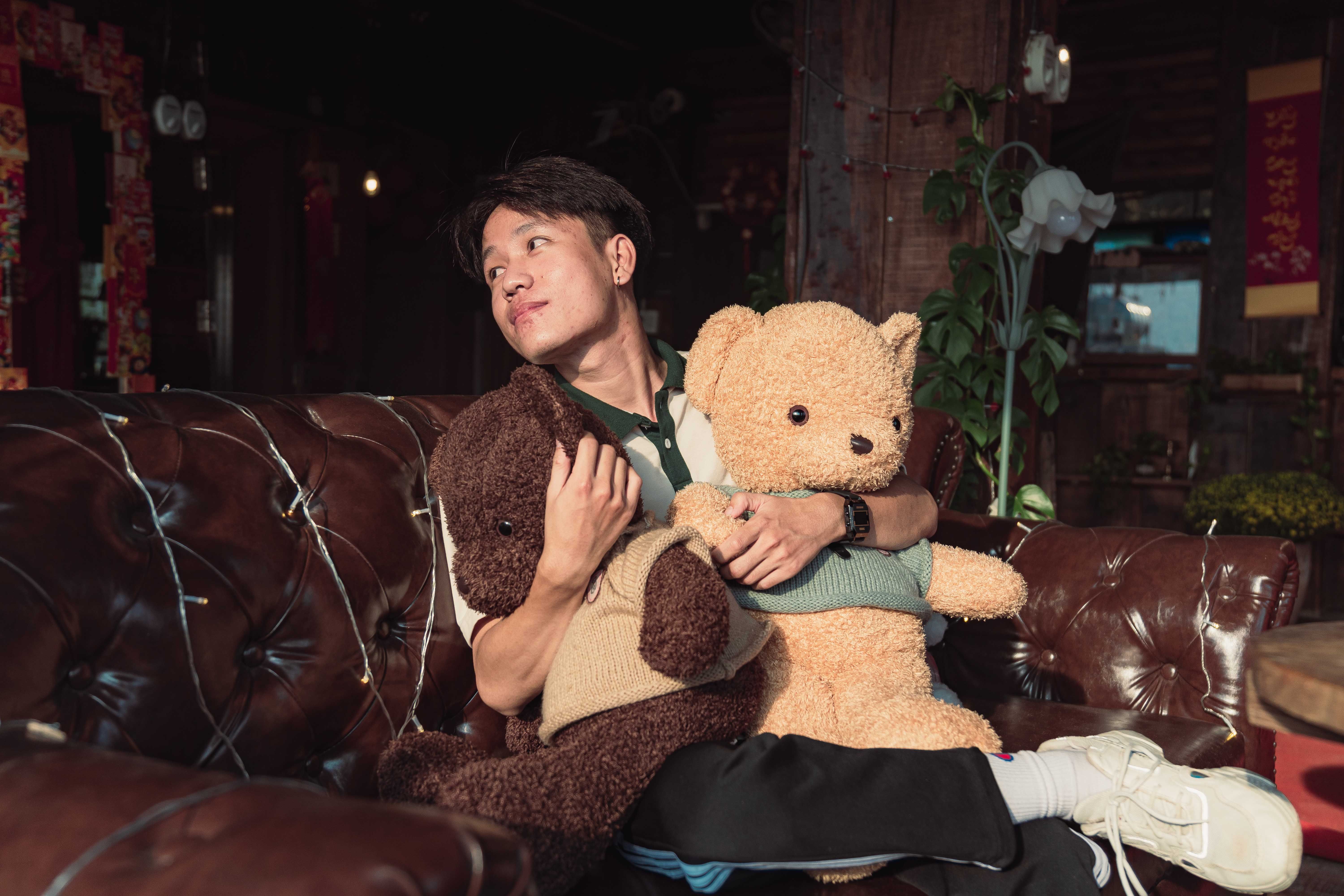 A young man relaxing with teddy bears on a leather sofa in a cozy indoor setting.