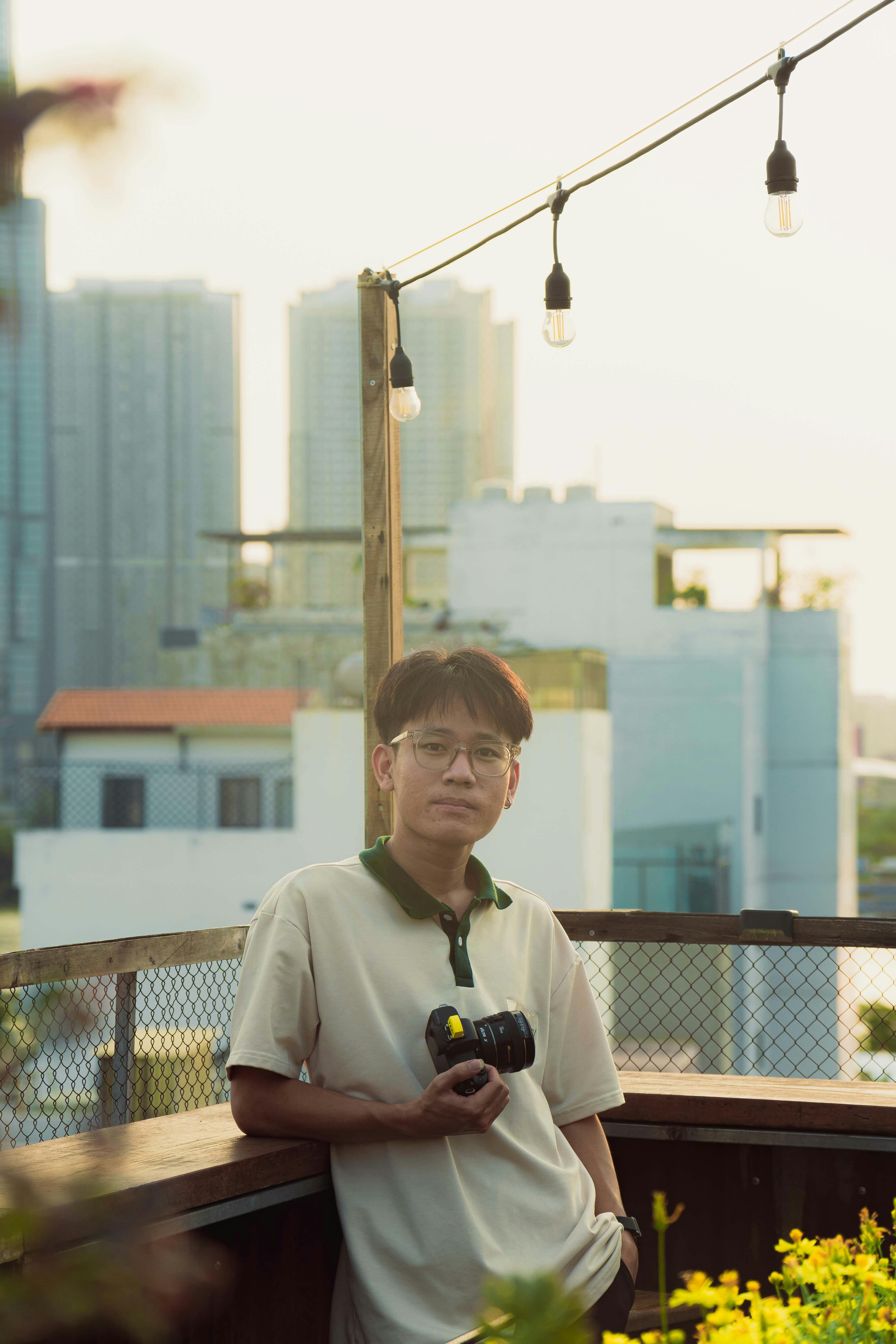 Portrait of a man holding a camera on a rooftop with a cityscape backdrop in Ho Chi Minh City.