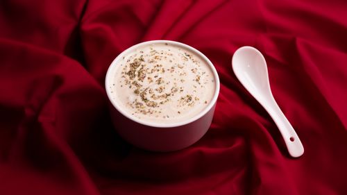 Free Elegant white bowl of creamy soup with herbs, set against a rich red fabric backdrop. Perfect for food photography. Stock Photo