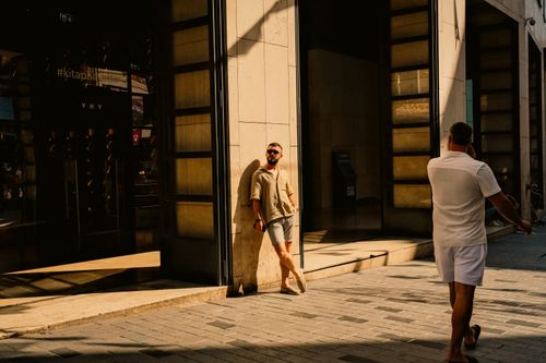 Free A man leans casually against a sunlit pillar on a city street, embodying urban relaxation. Stock Photo
