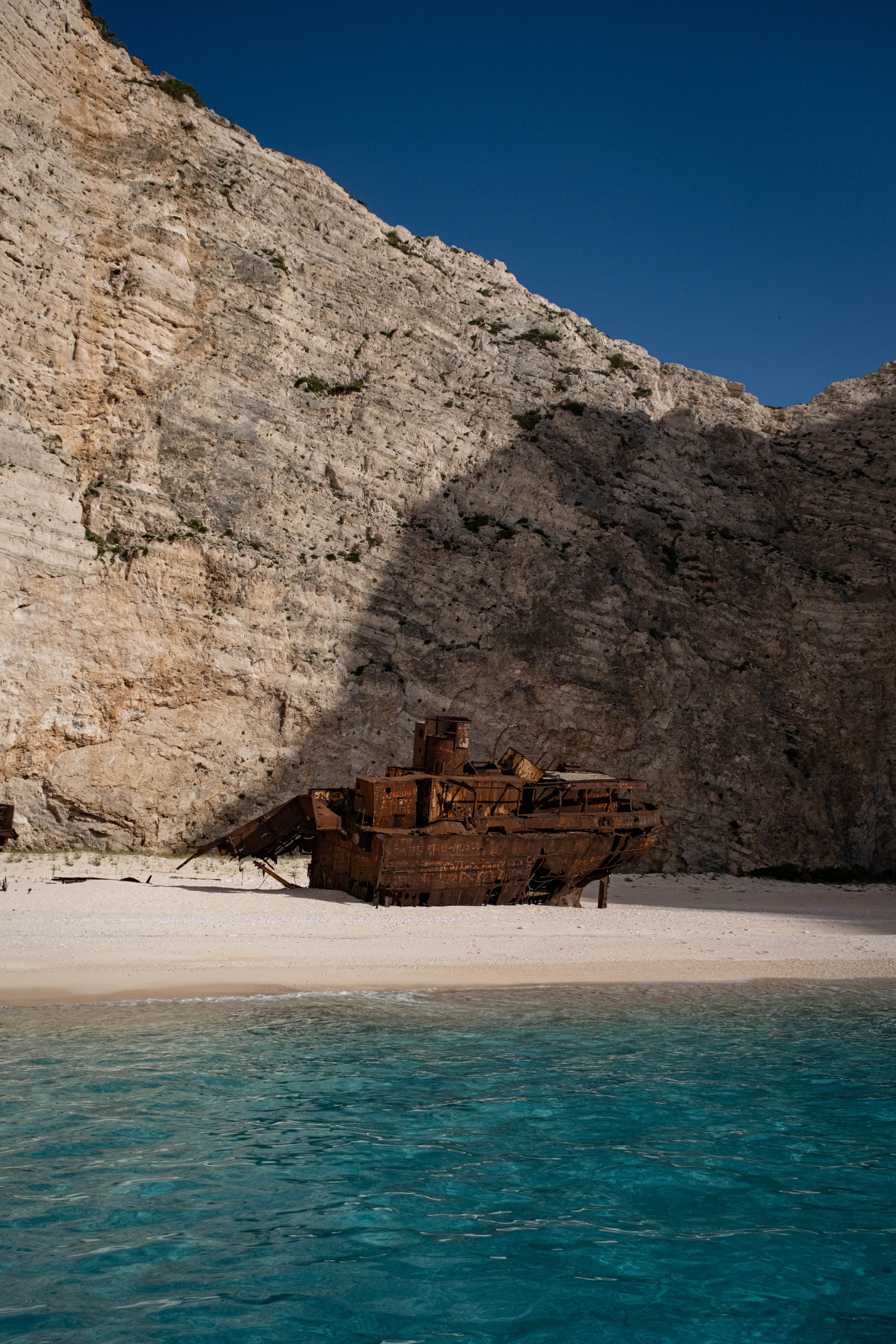 An old ship sits on the beach near a cliff · Free Stock Photo