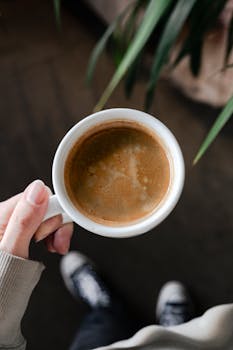 A hand holding a steaming cup of coffee with foam, captured from above.