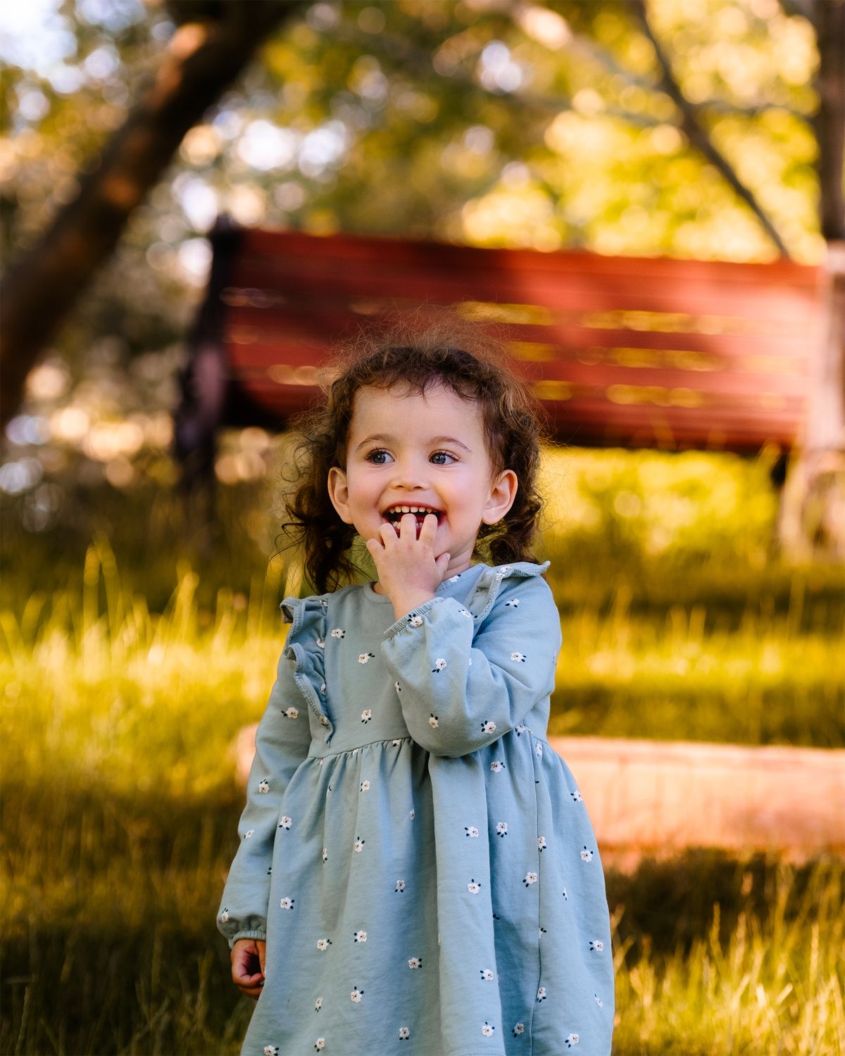 A little girl in a blue dress is standing in front of a bench · Free ...