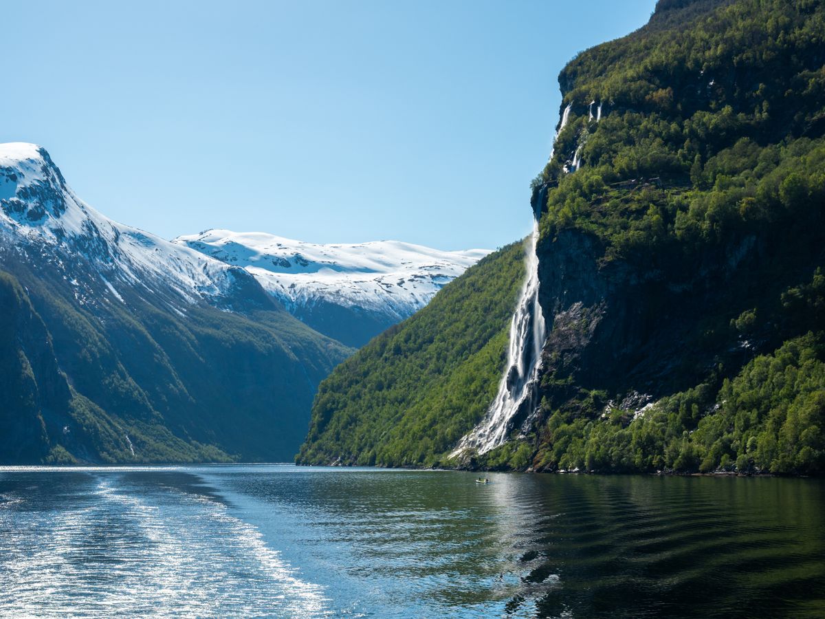 A tall waterfall dropping down the cliffs of Geirangerfjord seen from a ship's wake.