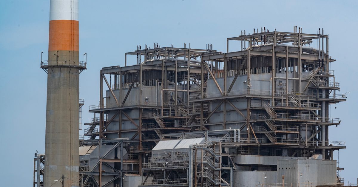 A power plant with smokestack on a sandy coastline, showcasing industrial architecture.