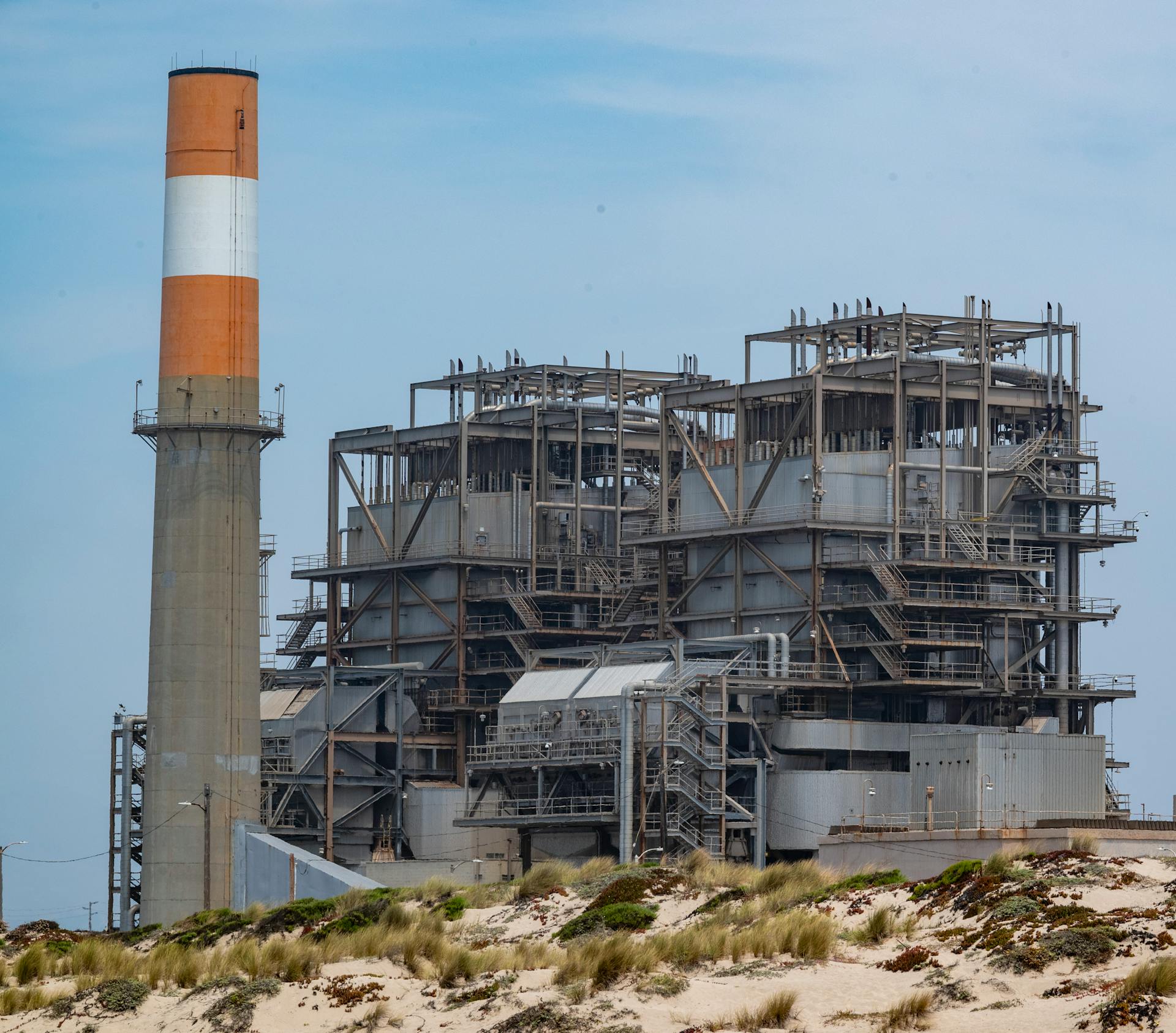 A power plant with smokestack on a sandy coastline, showcasing industrial architecture.