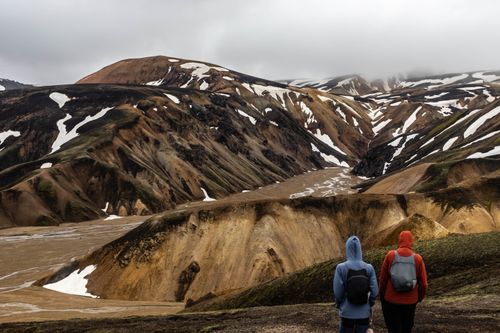 Free Two hikers explore the rugged and colorful mountains of Landmannalaugar, Iceland, under a cloudy sky. Stock Photo