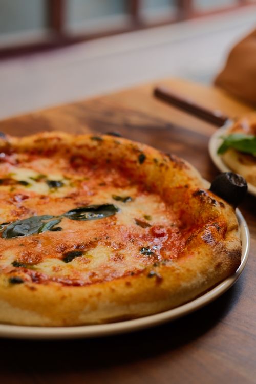 Free Close-up of mouth-watering homemade Margherita pizza with fresh basil on a wooden table. Stock Photo