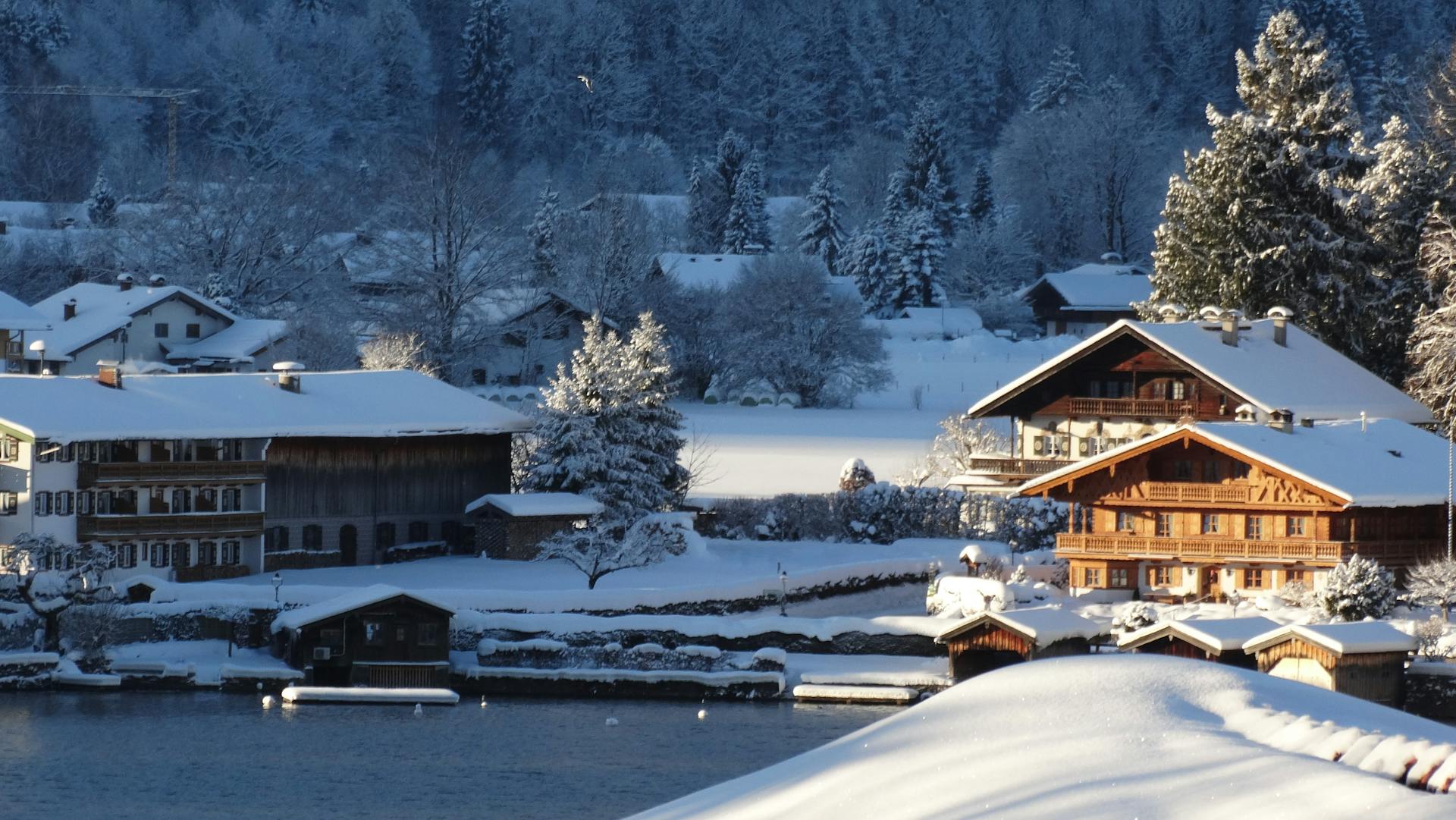 Picturesque winter scene featuring snow-covered chalets by a serene lake with frosty trees.