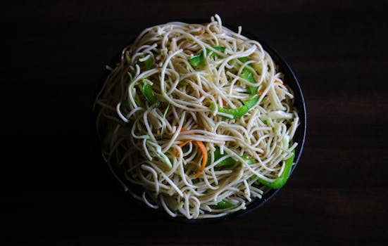 Tasty Indian-style Hakka noodles with vegetables in a dark, moody setting.