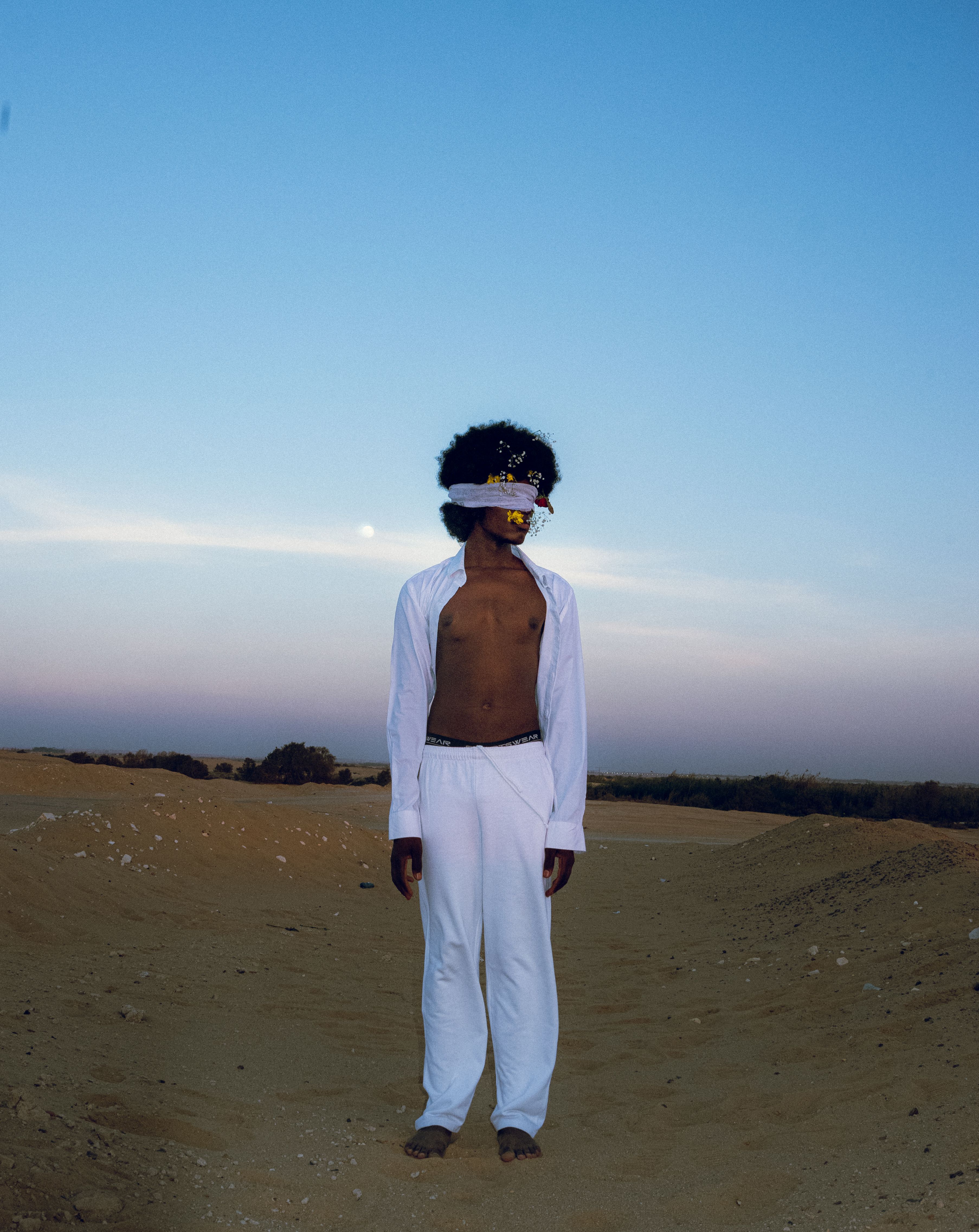 A man stands blindfolded in a desert under a twilight sky, embodying mystery and solitude.