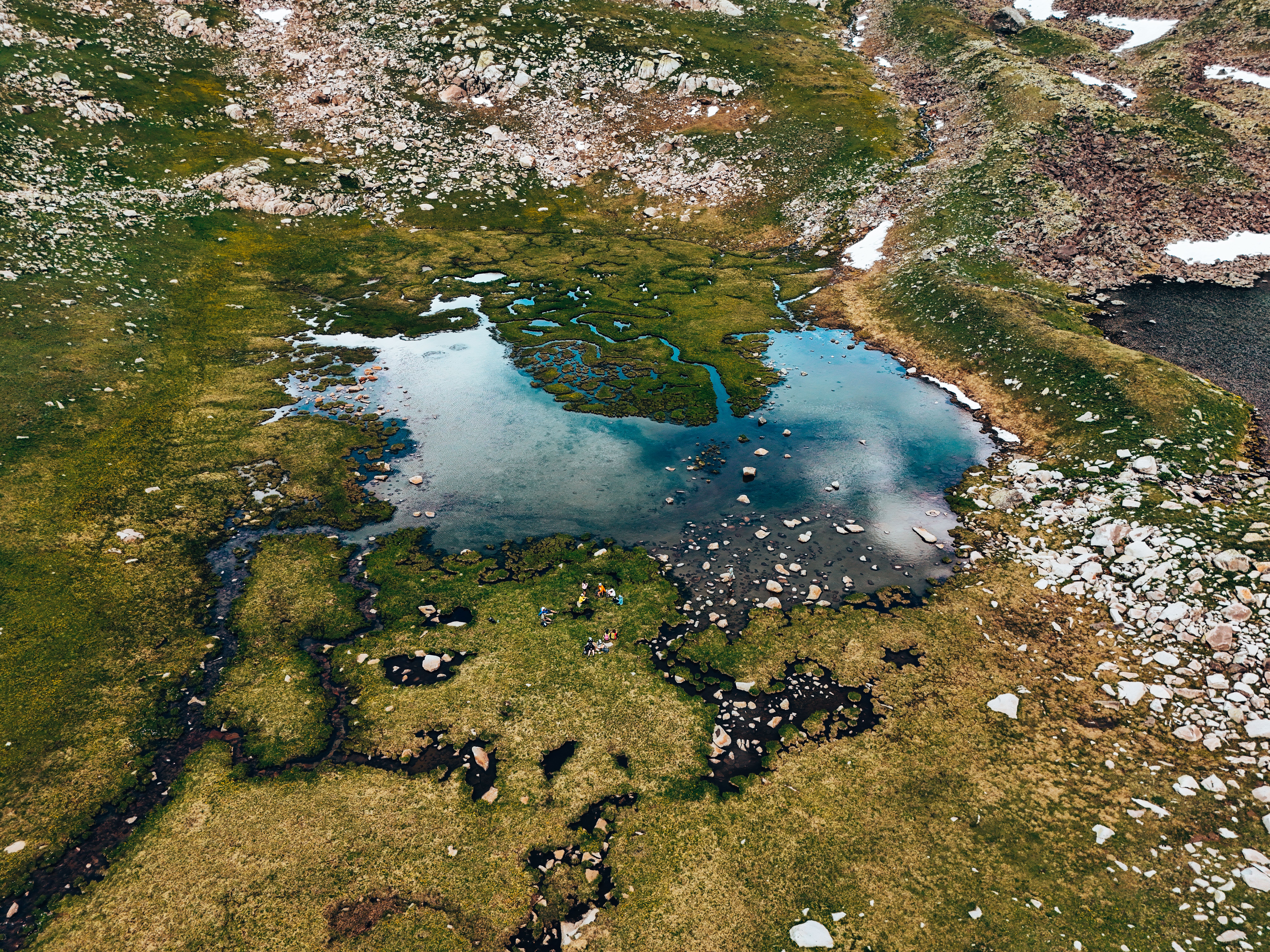 Aerial view of a serene pond surrounded by rugged landscape in İspir, Turkey, reflecting clear blue sky.