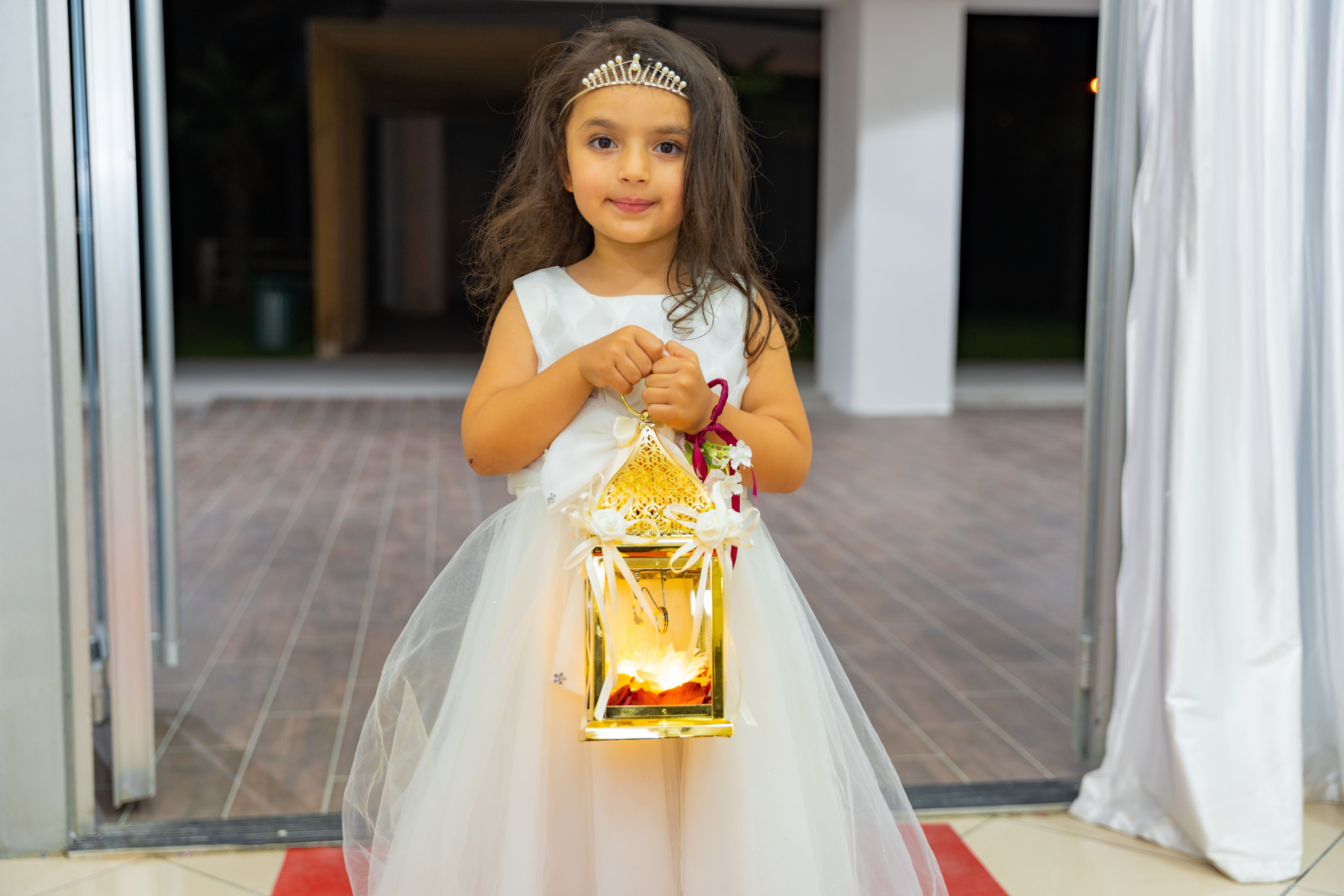 A young girl in a wedding dress holding a decorative lantern, ready to enchant the event.