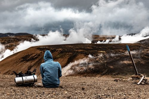 Free Person exploring the geothermal landscapes of Iceland, surrounded by steaming vents and rugged mountains. Stock Photo