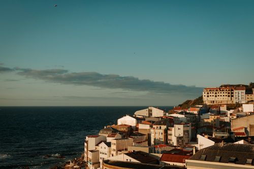 Free Stunning seaside view of Malpica, Spain with vibrant rooftops and the Atlantic Ocean at sunset. Stock Photo