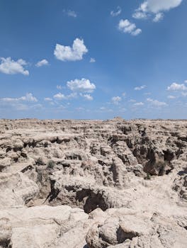 A vast rocky desert terrain under a clear blue sky with fluffy white clouds.