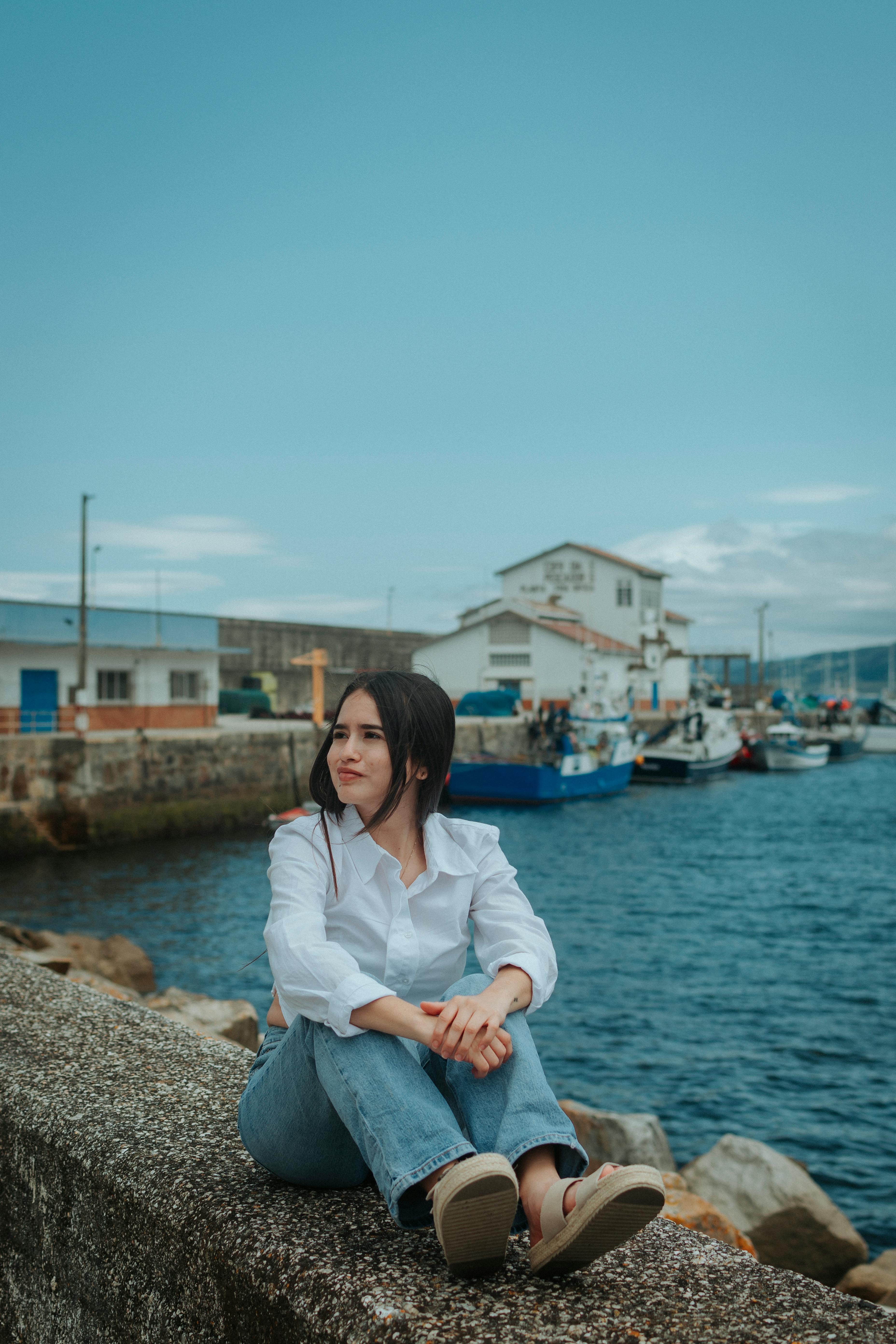 a woman sitting on a wall near a harbor