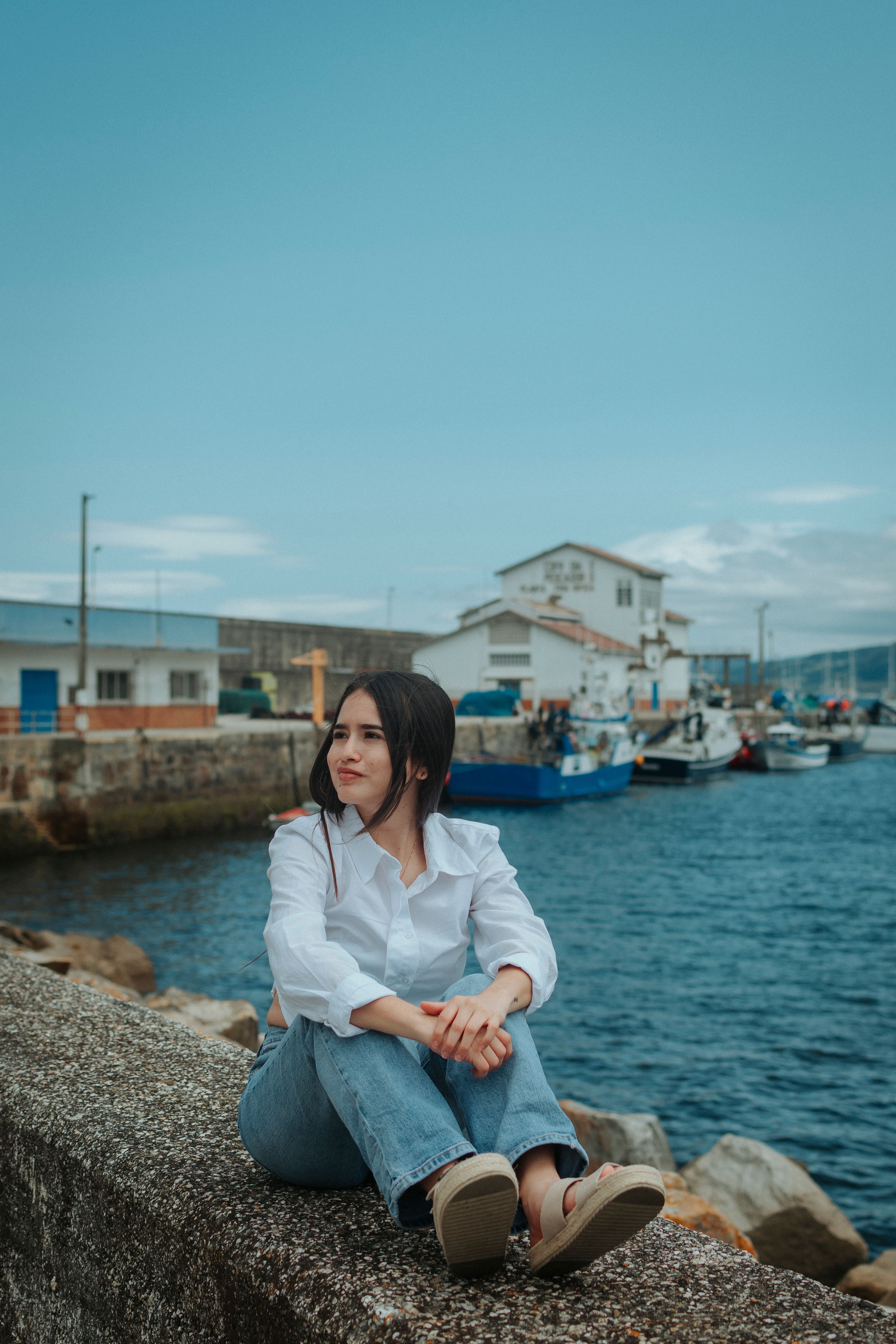 A woman sitting on a wall near a harbor · Free Stock Photo