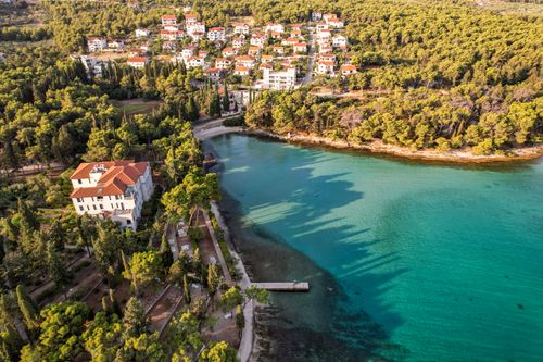 Free Aerial view of a picturesque coastal town surrounded by dense forests and clear turquoise waters. Stock Photo