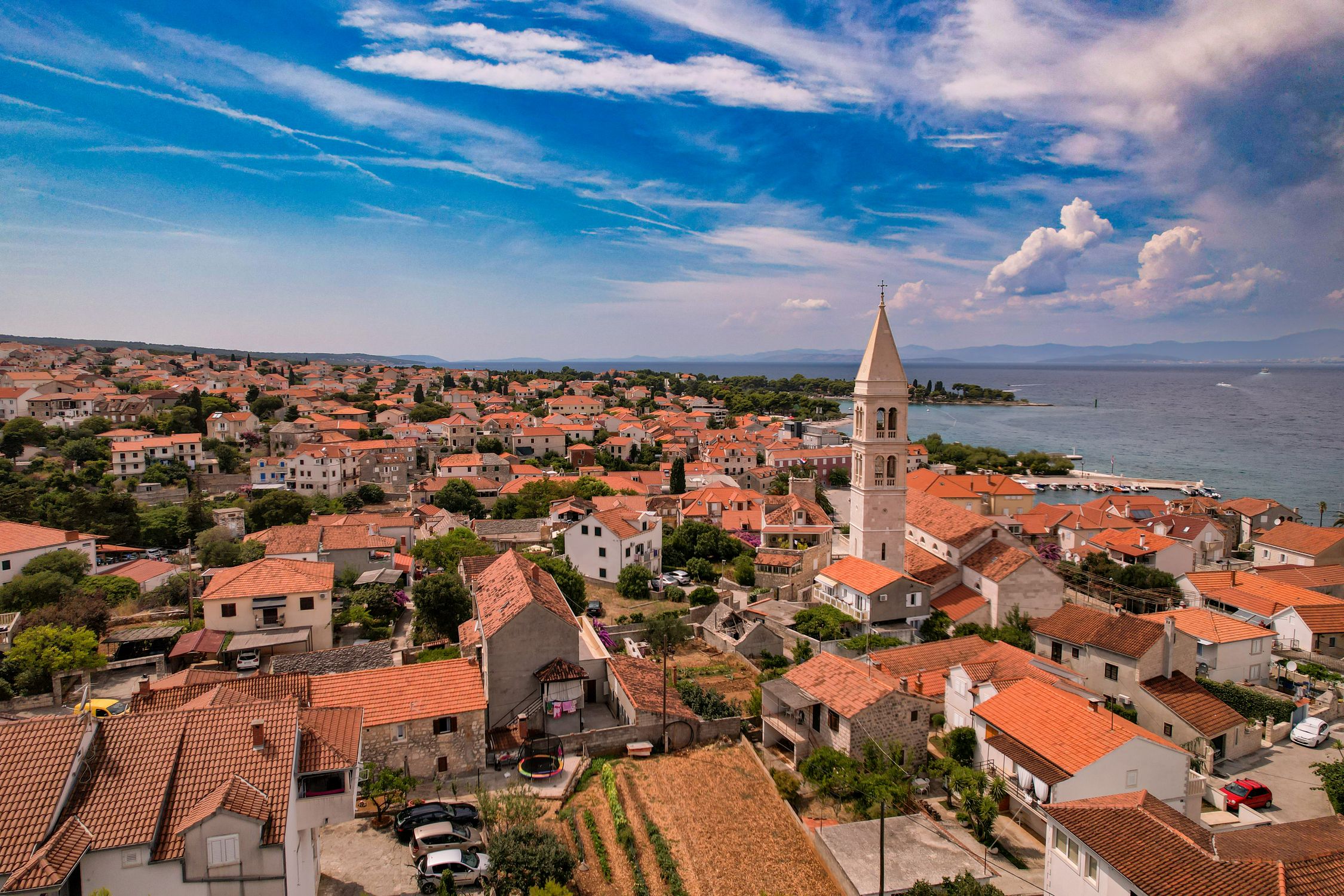 A picturesque aerial view of a coastal town with orange rooftops and church tower under a vibrant sky