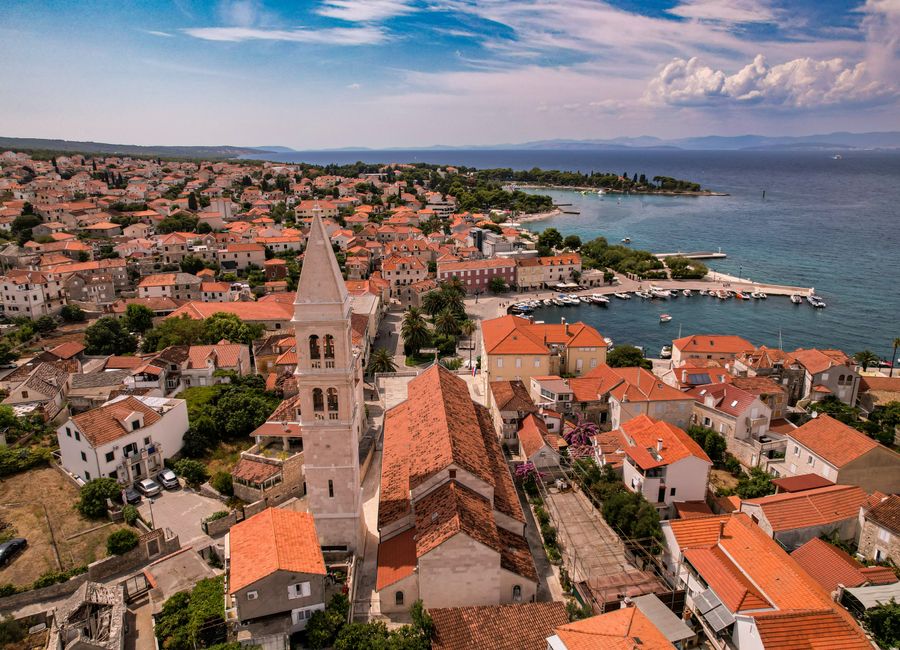 A scenic aerial view of a coastal town featuring a historic church tower and red-roofed buildings by the sea.