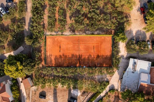 Free High-angle shot of a clay tennis court amidst trees and rustic surroundings, capturing a serene summer scene. Stock Photo