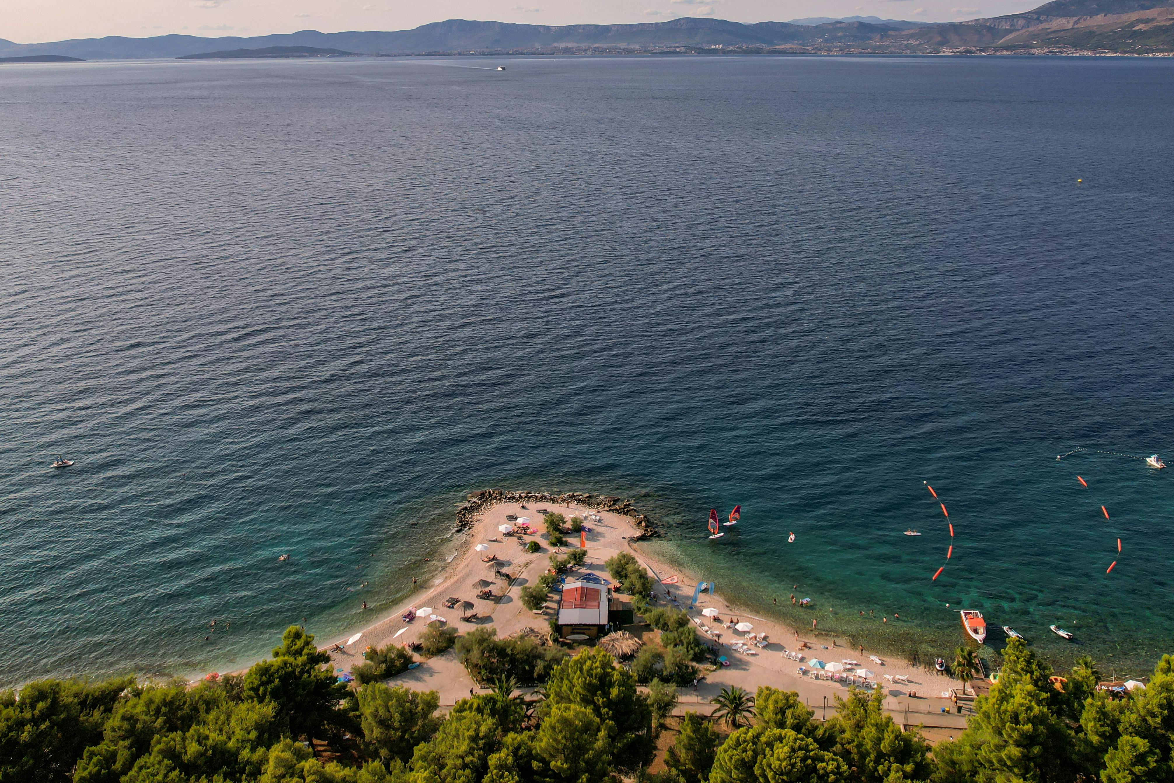 Prescription Goggle Inserts - Aerial view of a picturesque beach and peninsula surrounded by calm ocean waters and distant mountains.