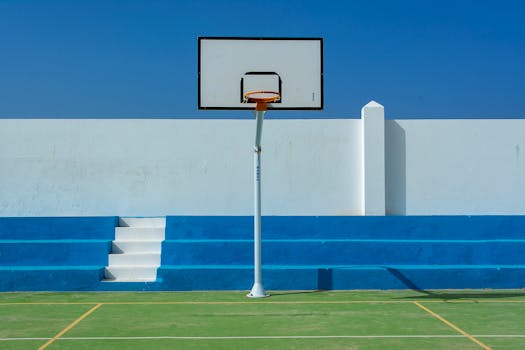 Minimalist outdoor basketball court with a hoop and striking blue stands under a clear sky.
