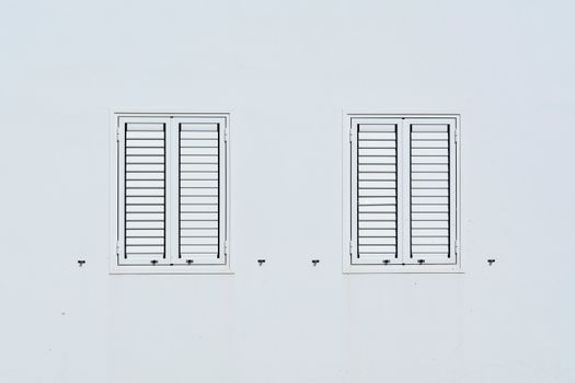 A minimalist design featuring two shuttered windows on a white wall, emphasizing simplicity and space.
