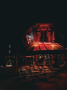 A charming Parisian café, Chez Ginette, illuminated by neon lights at night.