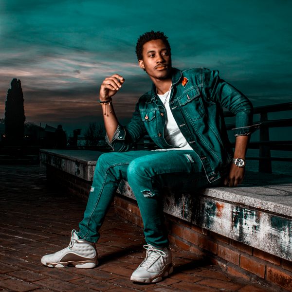 A man in a denim jacket sitting on a concrete slab — photo by Lucxama Sylvain on Pexels