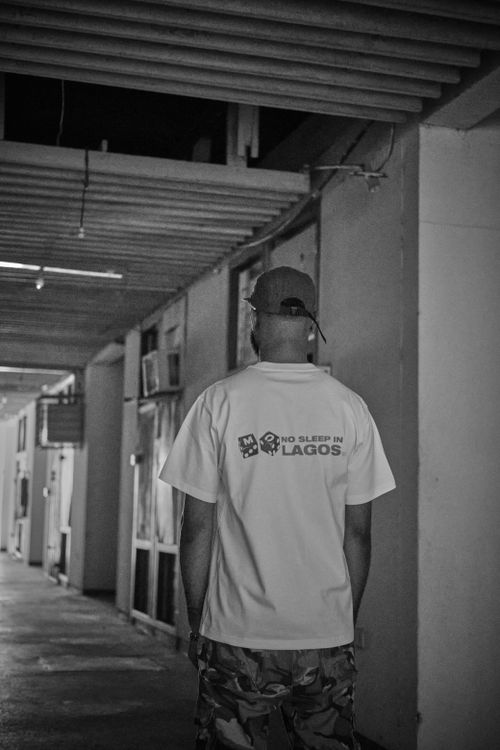 Free A man in a white 'No Sleep in Lagos' t-shirt and camouflage pants walking indoors. Stock Photo
