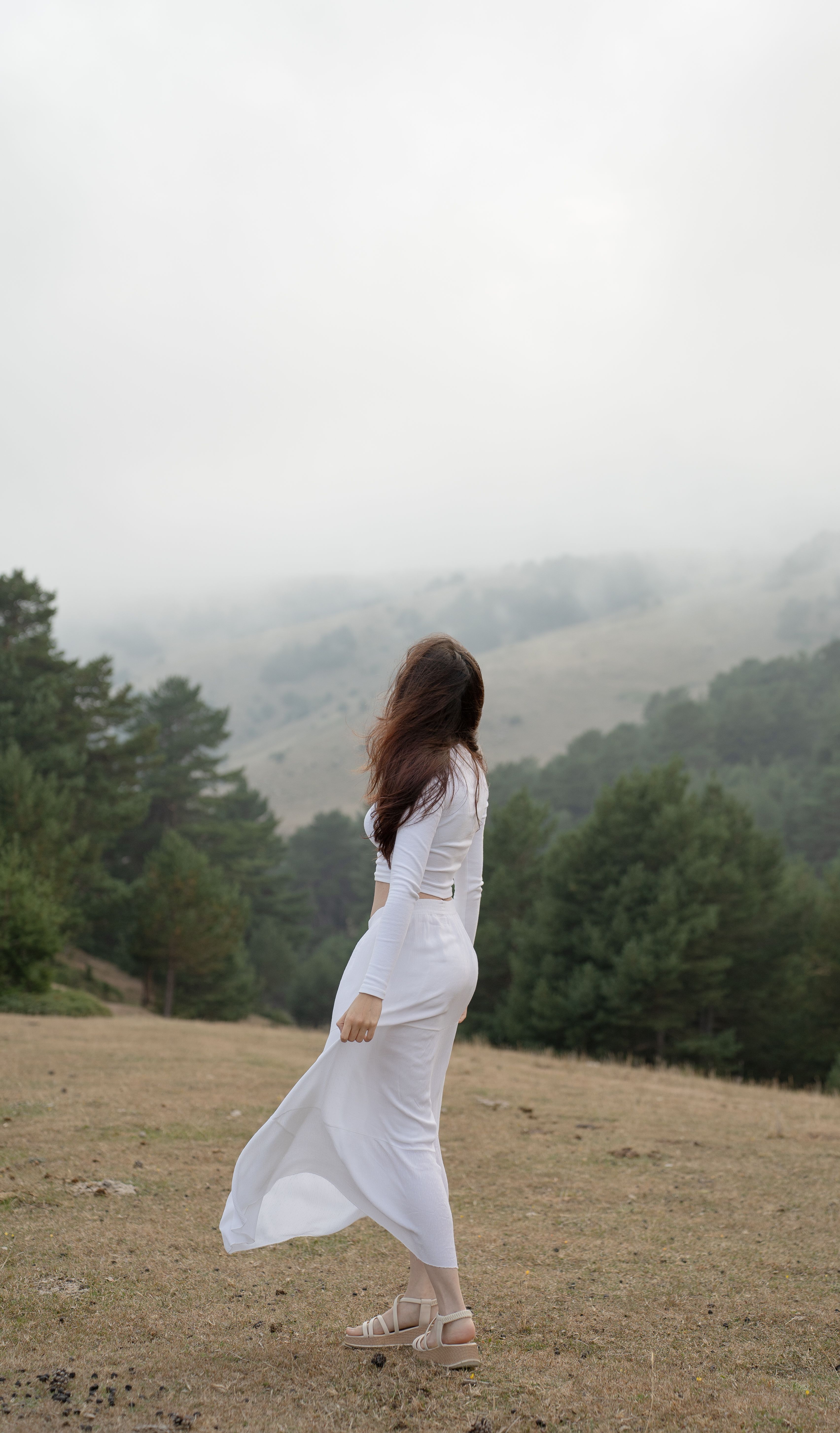 Woman in white dress enjoys serene misty outdoor scene with lush greenery.