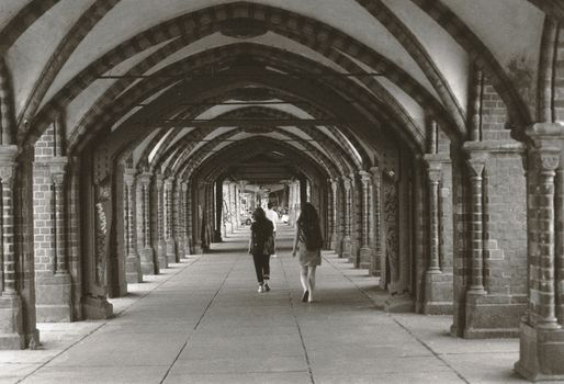 Two people walking under an arched walkway