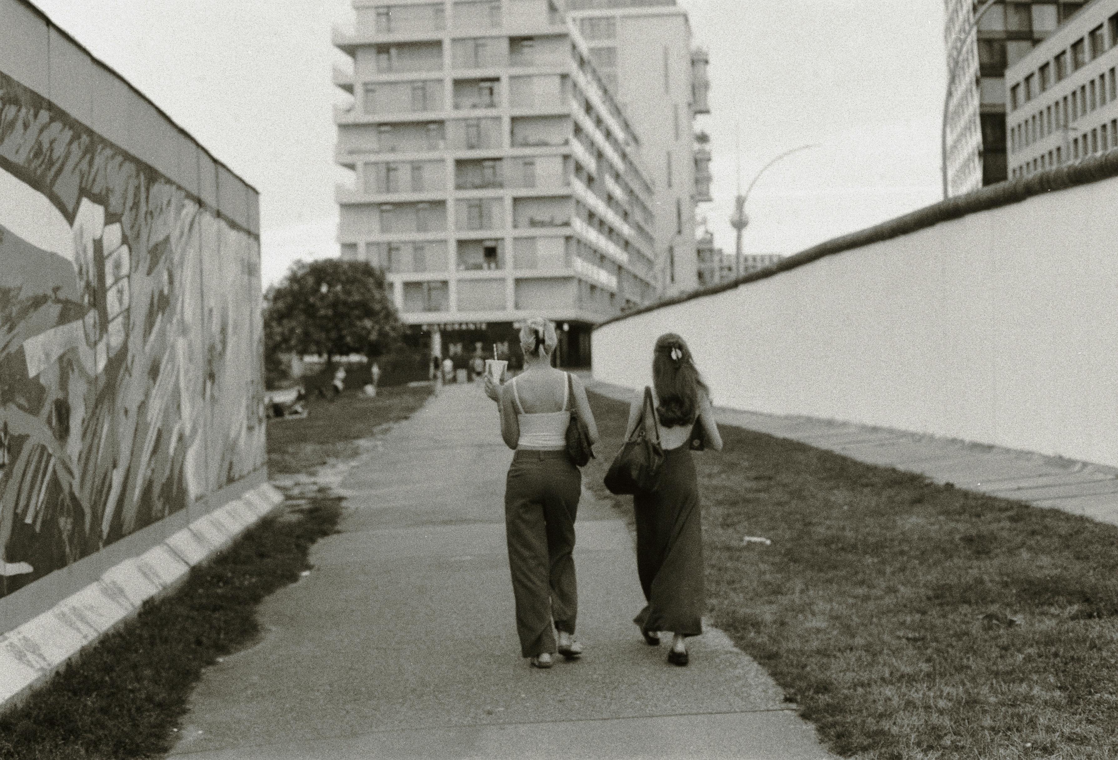 Black and white photo of two women walking alongside the Berlin Wall in Berlin, Germany.