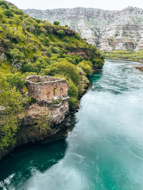 Free River flowing past ancient ruins surrounded by lush greenery in a mountainous region. Stock Photo