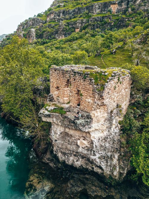 Free Explore ancient ruins perched on a rocky cliffside above a tranquil river in Turkey. Stock Photo