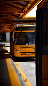 Yellow city bus parked at an outdoor urban station terminal during the day.