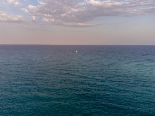 Free Peaceful expanse of ocean at dusk with a lone sailboat on the horizon near Casablanca, Spain. Stock Photo