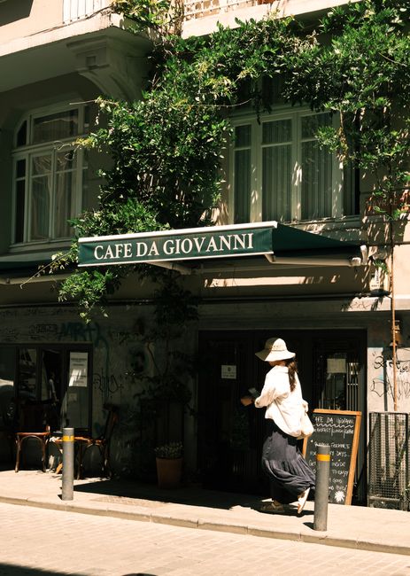 Charming street view of Cihangir with a cafe and a woman walking by under the sun.