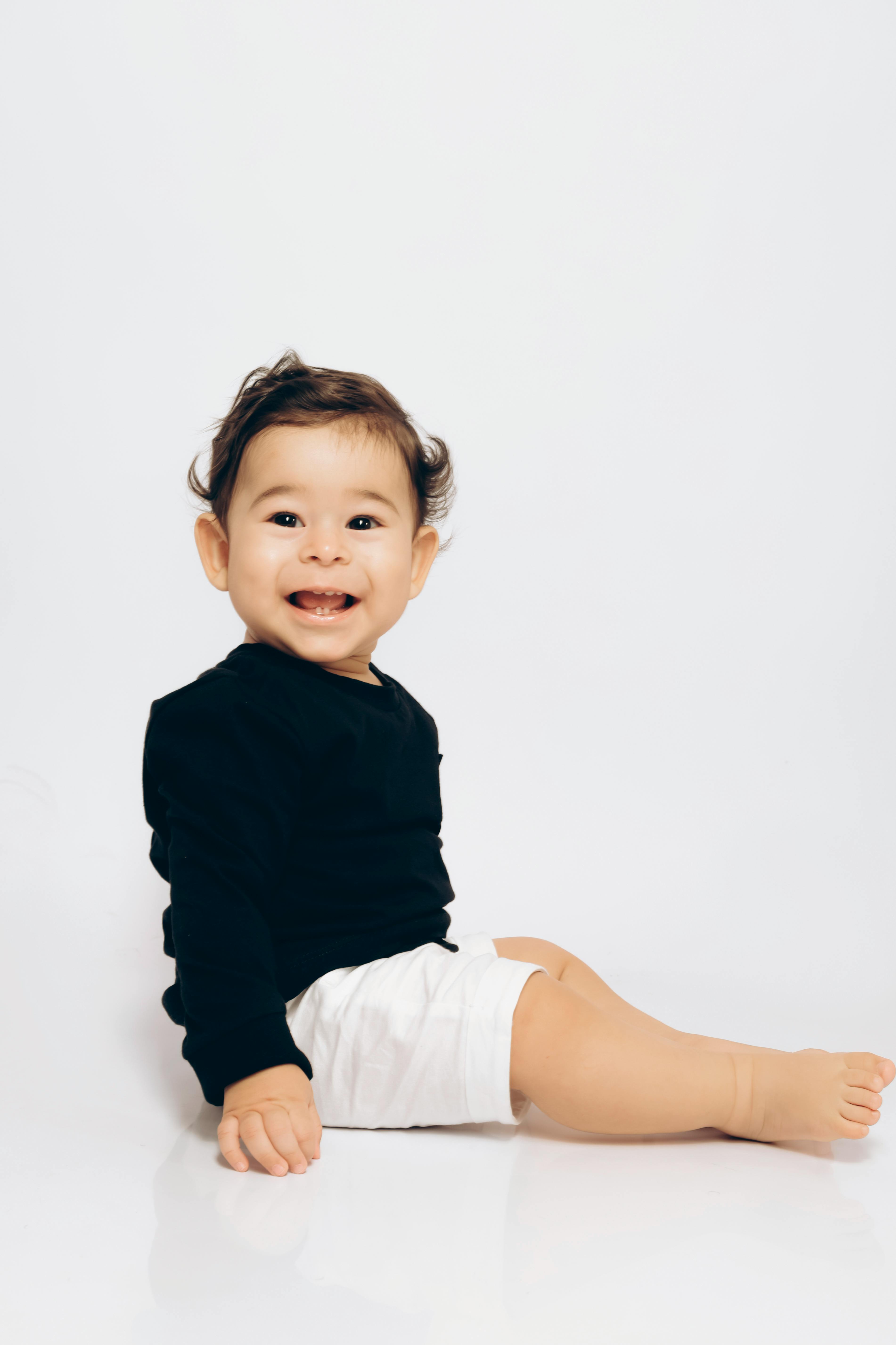 Cute baby sitting on the floor, smiling joyfully in a black outfit. Perfect portrait of innocence.