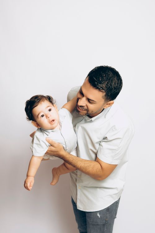 Free Father lovingly holding his young child, both dressed casually, against a simple white backdrop. Stock Photo