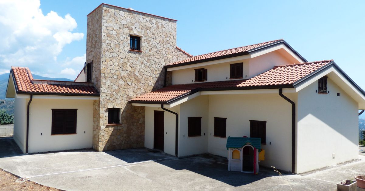Spacious family house featuring a stone facade and red tile roof, set outdoors under a bright blue sky.