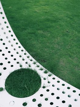 Modern abstract design with grass and perforated white surface outdoors.