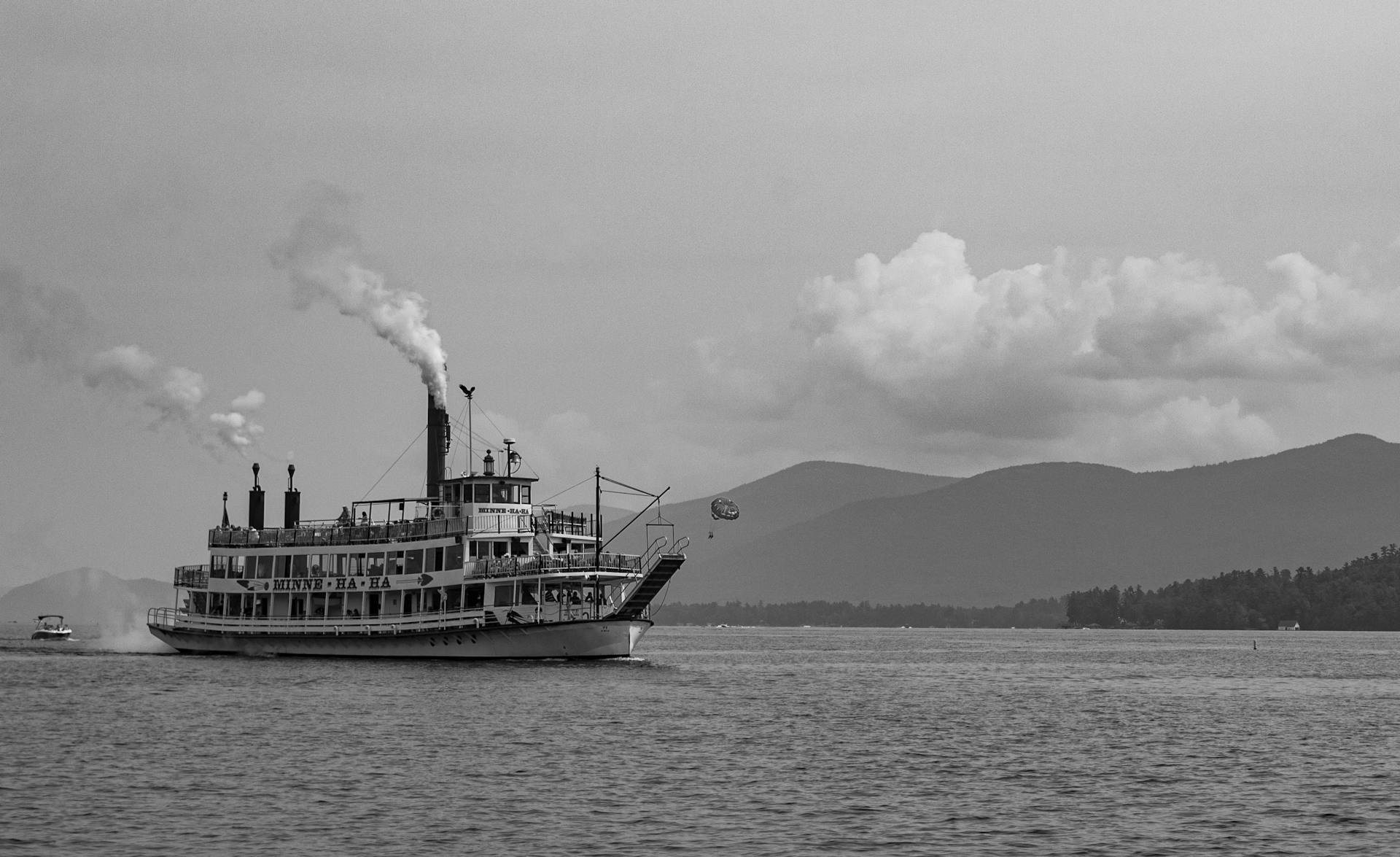 A vintage steamboat sails gracefully on a tranquil lake with mountain views in black and white.