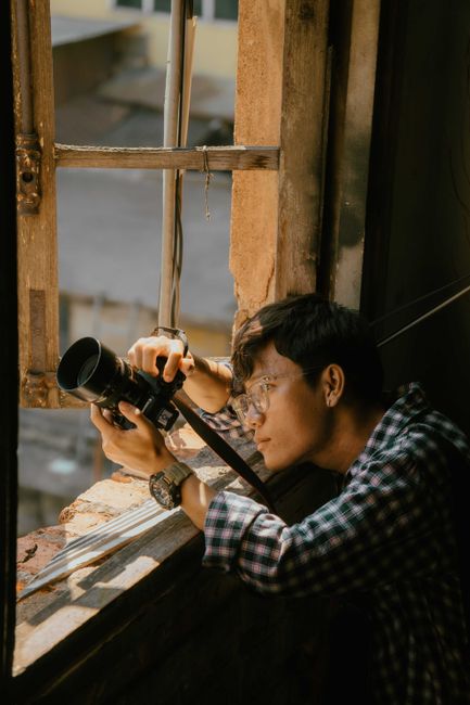 A young man capturing the cityscape from a rustic window in Ho Chi Minh City, Vietnam.