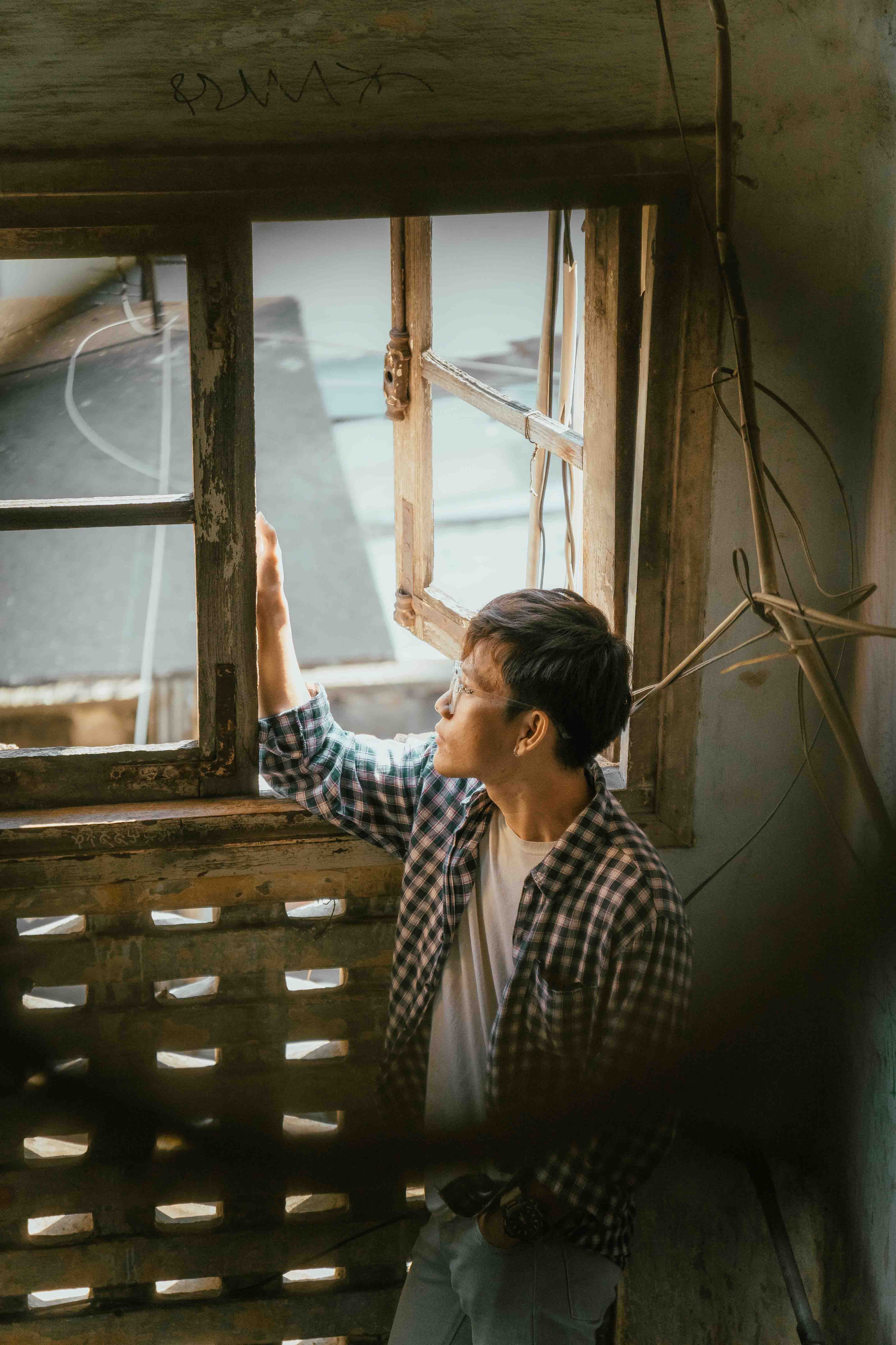 A man stands by a weathered window, deep in thought, in an abandoned building.