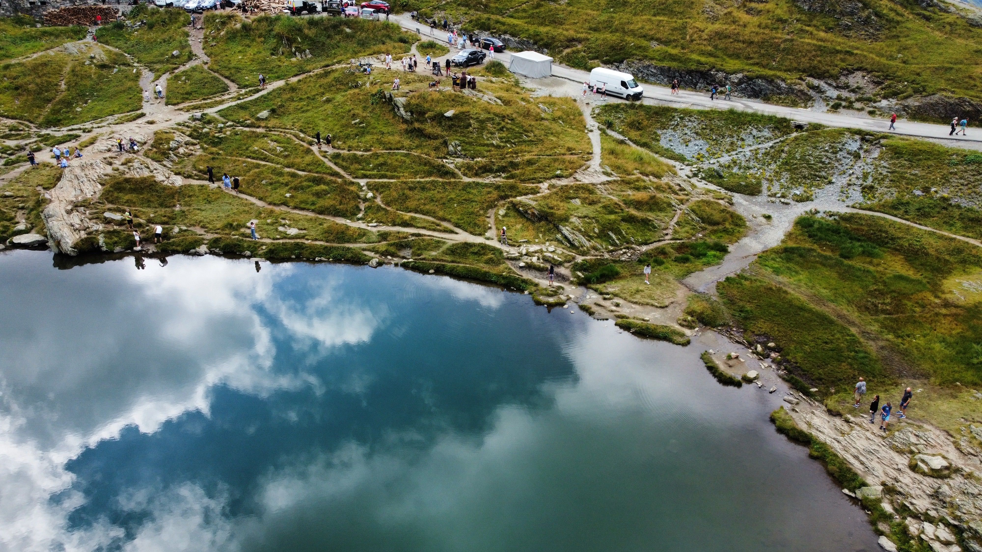 A picturesque aerial view of a serene lake surrounded by lush greenery and hiking trails reflecting the cloudy sky.