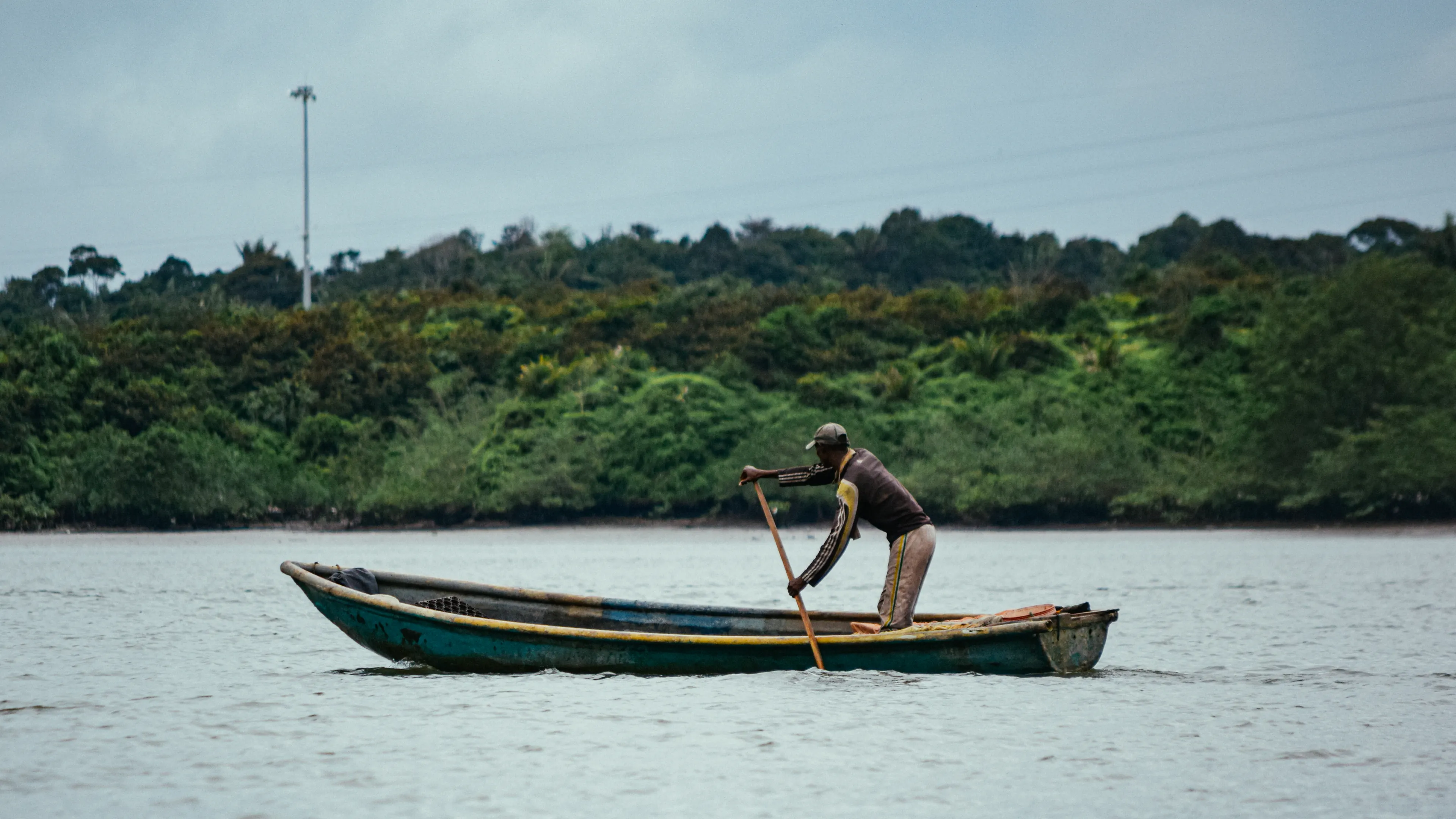 A fisherman paddles his canoe on a serene river in Buenaventura, Colombia, surrounded by lush greenery.