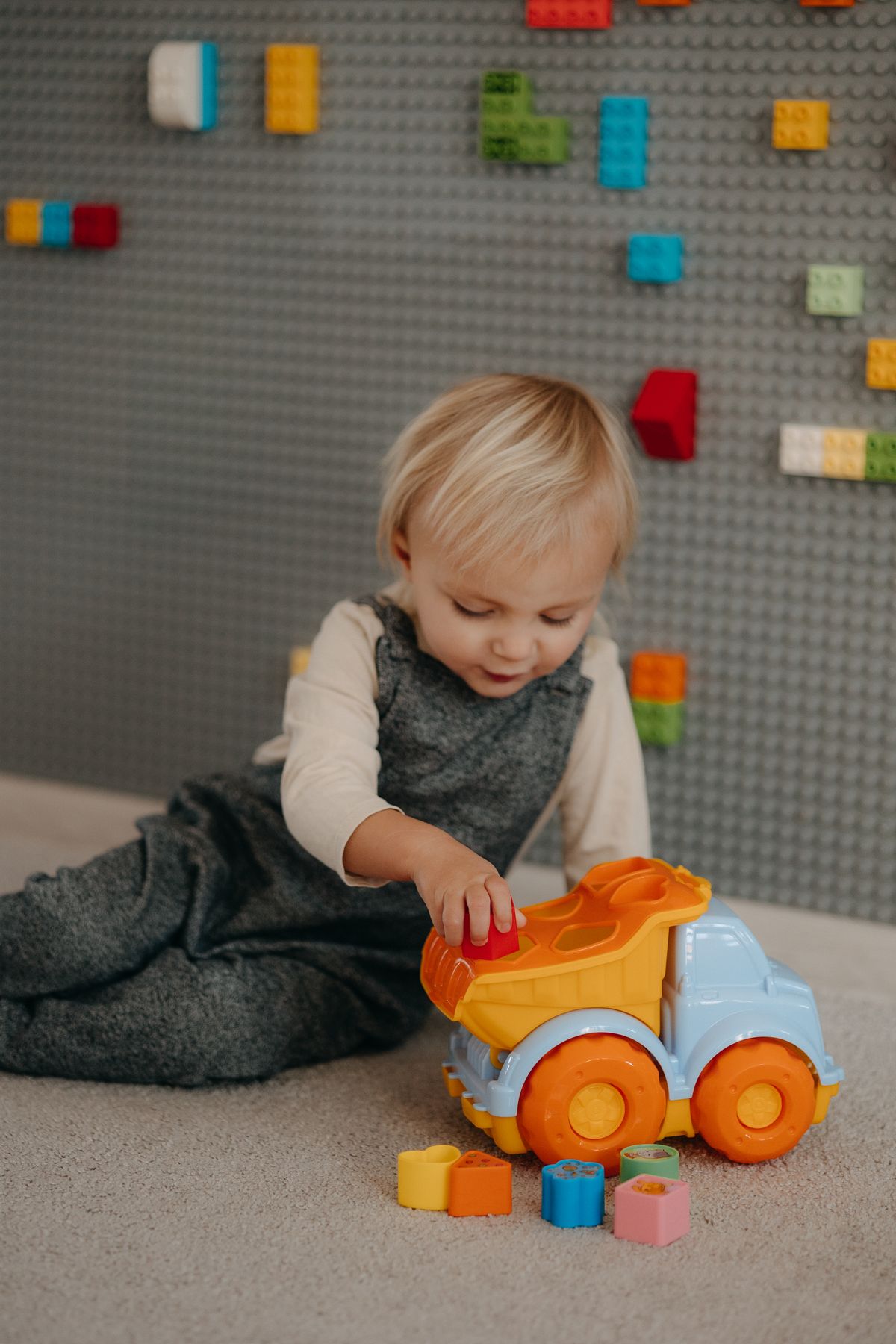 A cute toddler playing with a colorful toy truck and building blocks stored together in a vehicle bin